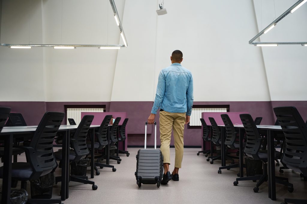 Man with a suitcase standing in the middle of an empty office room.